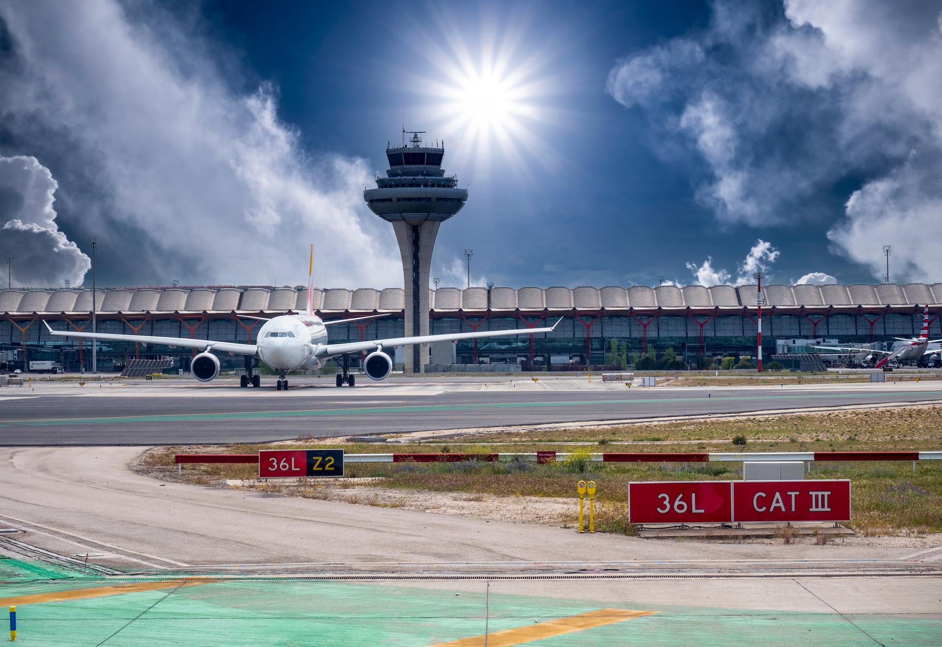 An airplane is parked outside of an air traffic control tower on a sunny day.