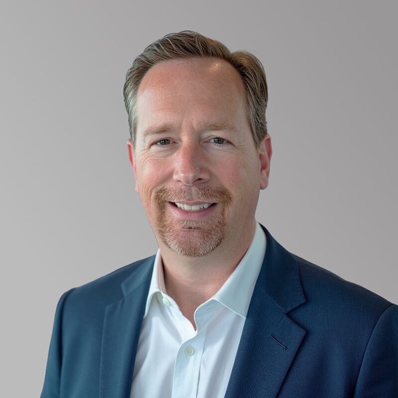 Aaron Lax has a relaxed smile and auburn hair. He's wearing a fine blue suit jacket with a white collared shirt.